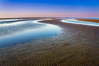 The wave pattern on the sand was softly lit as the sun sets in Bolivar Peninsula in Texas.