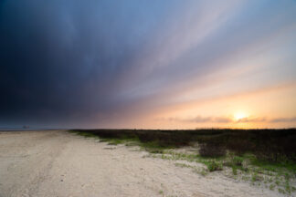 As the rain clouds approached to the shore, the sunset colors blended in the dark sky at Bolivar Flats in Texas.