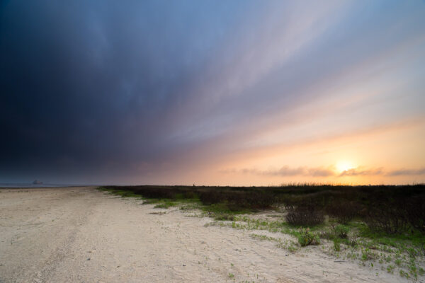 As the rain clouds approached to the shore, the sunset colors blended in the dark sky at Bolivar Flats in Texas.