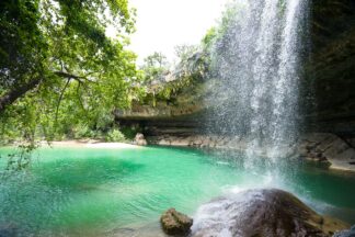 The waterfall flows into the beautiful emerald green natural swimming hole at Hamilton Pool Preserve in Dripping Springs, Texas, giving refreshing cool sprays.