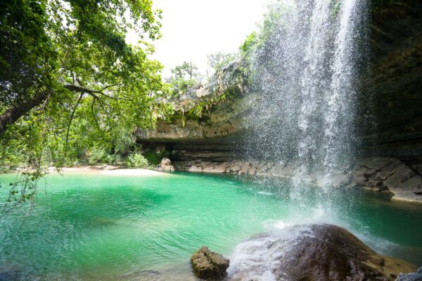 The waterfall flows into the beautiful emerald green natural swimming hole at Hamilton Pool Preserve in Dripping Springs, Texas, giving refreshing cool sprays.