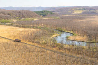 A train travels by the Kushiro River in the middle of Kushiro Shitsugen National Park in the early spring.